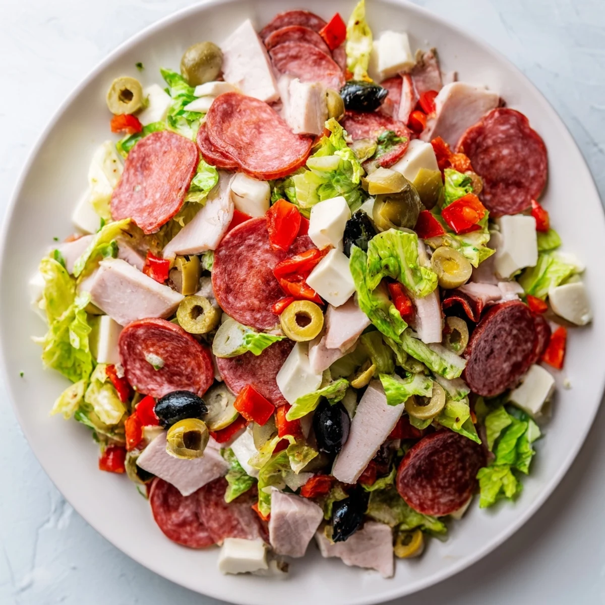 Brightly colored New Orleans Muffuletta Salad in a white bowl with halal meats, olives, and mozzarella.