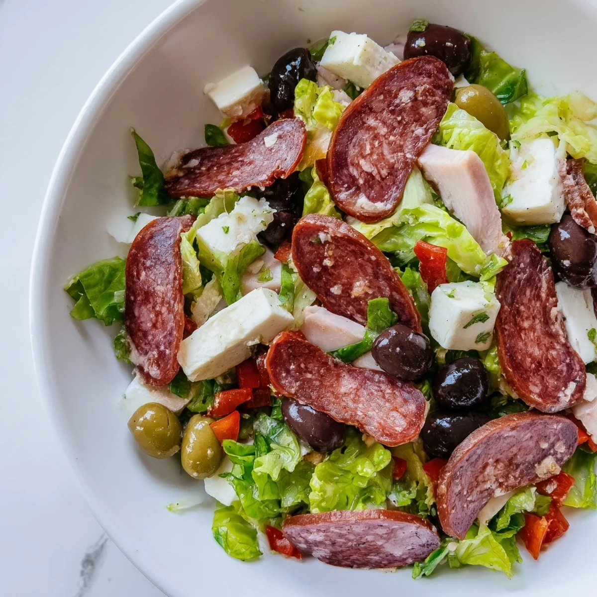 Layers of New Orleans Muffuletta Salad with cherry tomatoes, cucumbers, and crunchy pickled giardiniera.