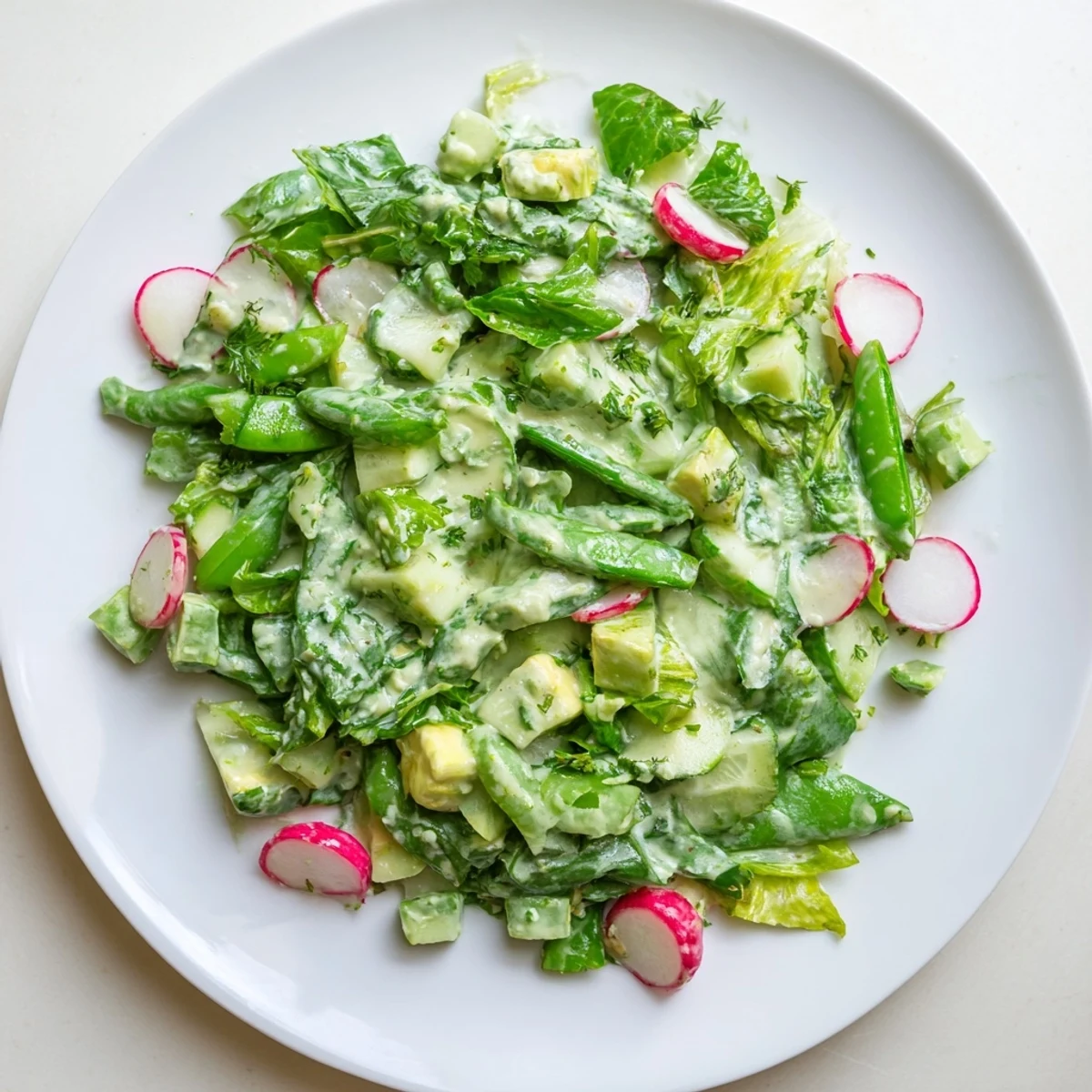 A close-up of Green Goddess Salad with avocado dressing, ready to serve with a sprinkle of fresh herbs and lemon.