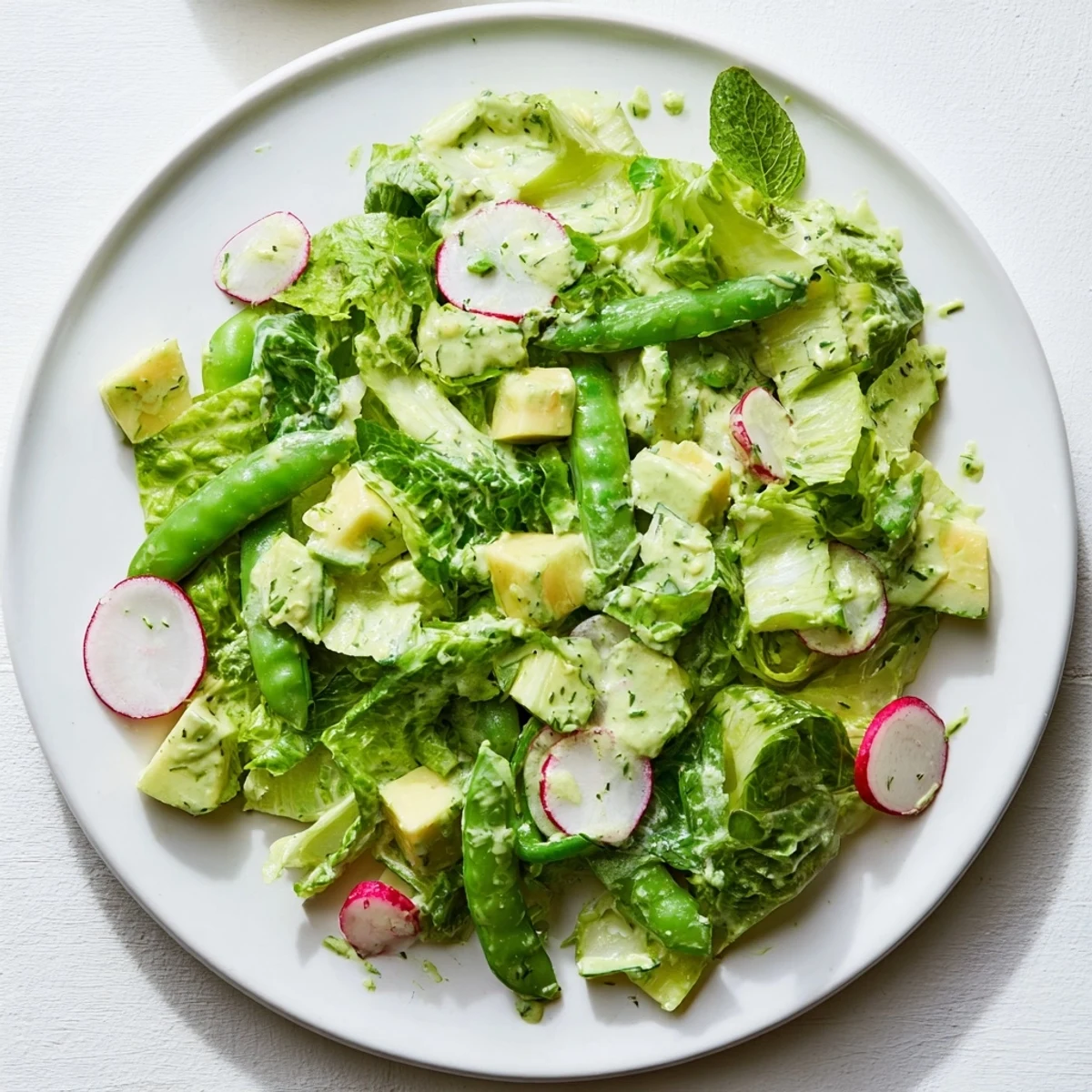 Freshly blended Green Goddess Salad with avocado dressing featuring crisp romaine, cucumber, and radishes tossed in vibrant green sauce.