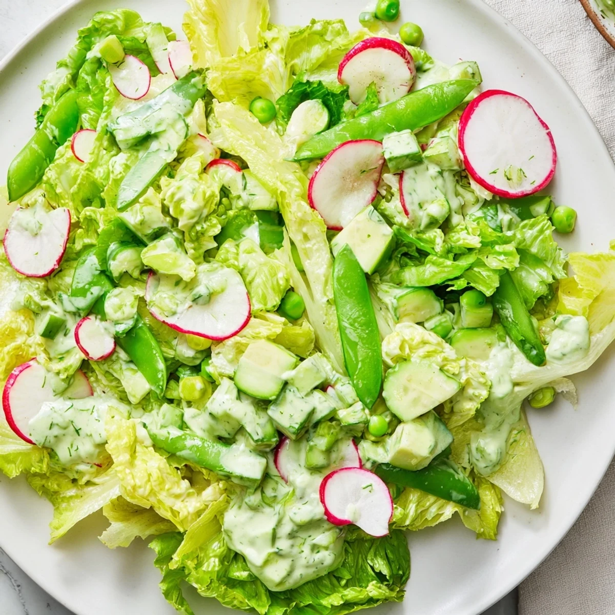 Healthy vegetarian Green Goddess Salad with avocado dressing, showcasing snap peas, spinach, and creamy dressing for a light lunch.