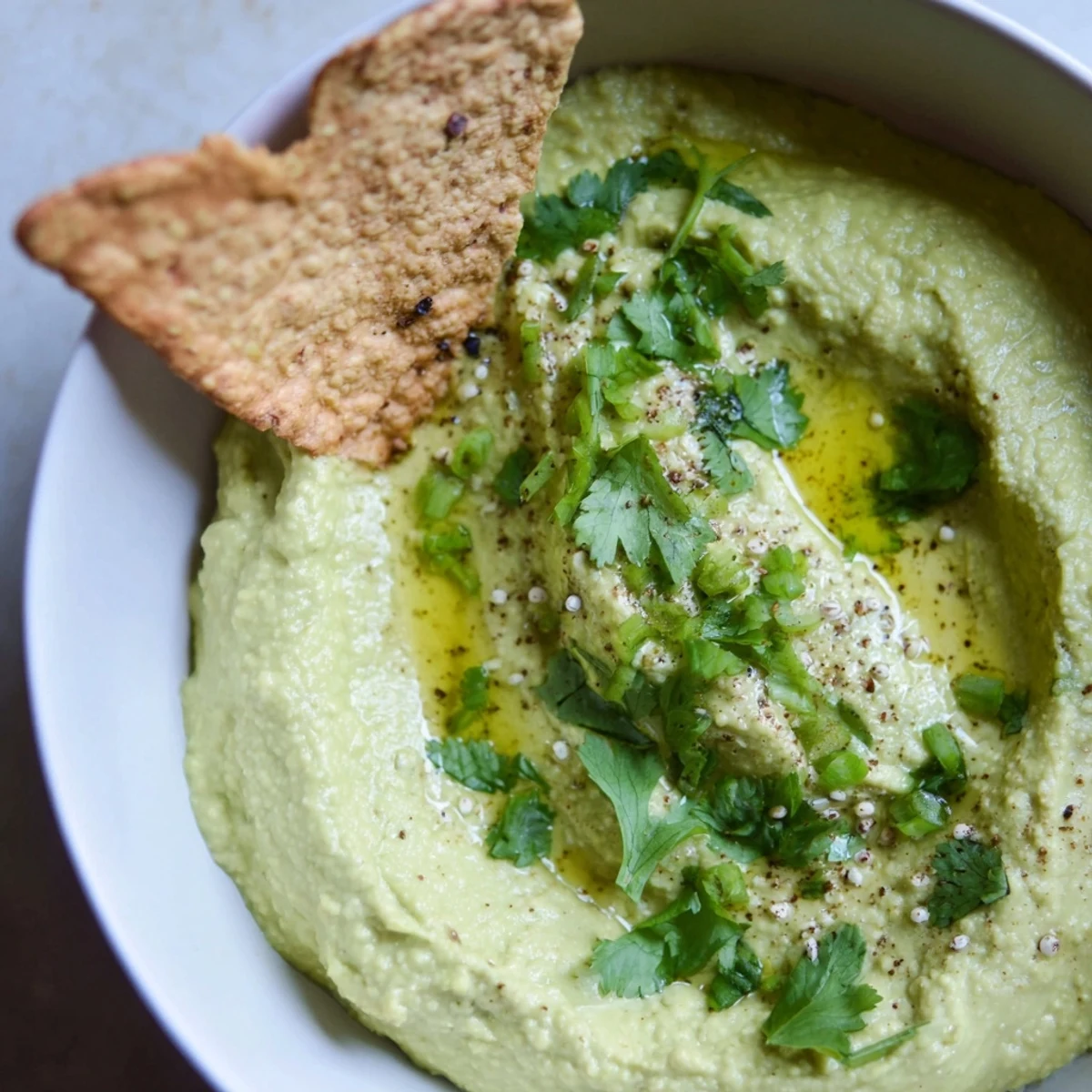 Close-up of crisp, golden-baked Pita Chips being dipped into vibrant Green Avocado Hummus.