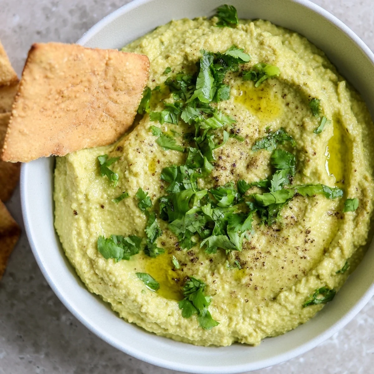 Appetizer platter of Green Avocado Hummus with Pita Chips, garnished with cilantro and lime wedges.