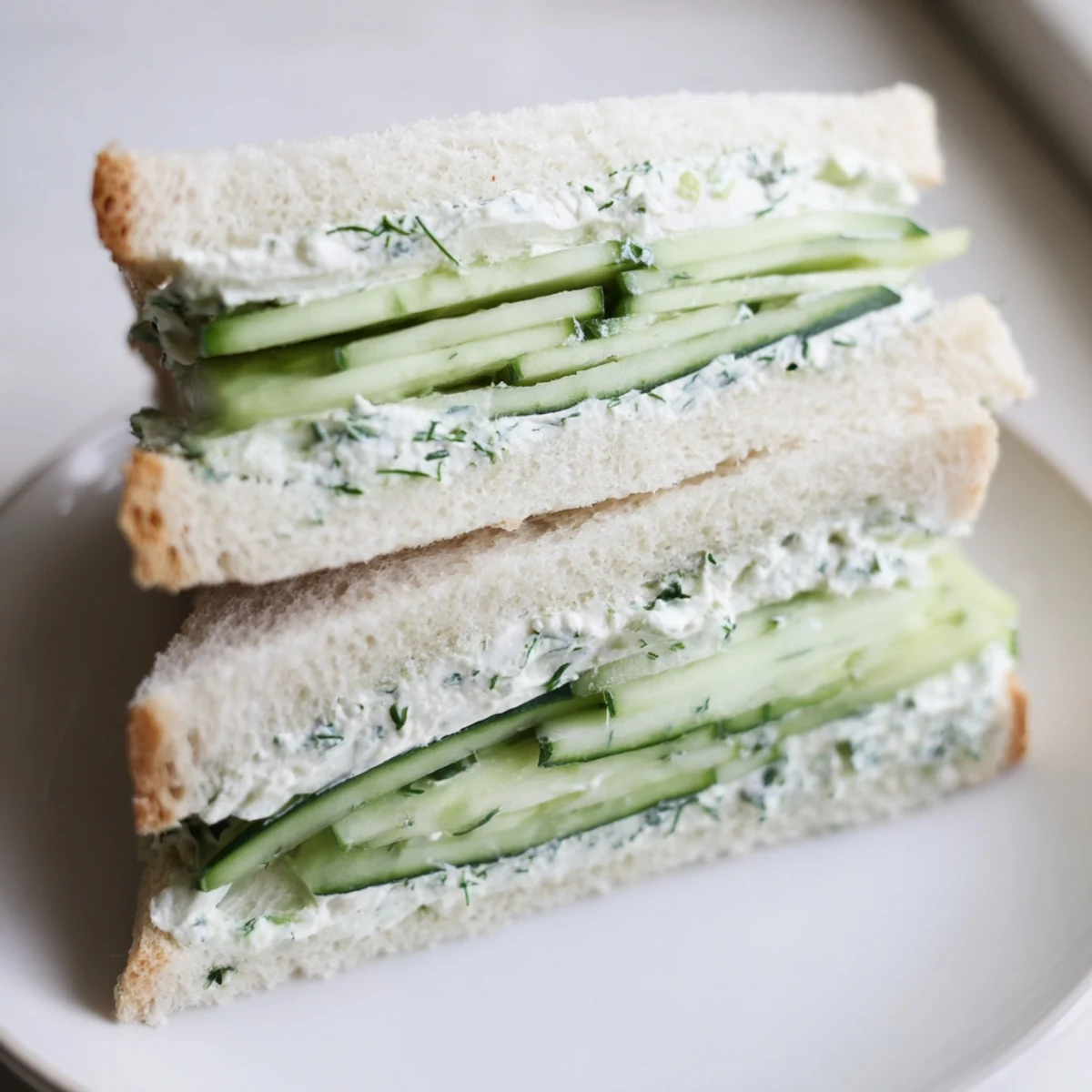 A close-up of cucumber sandwiches with herb cream cheese, showing crisp cucumber slices and a creamy green-flecked spread.  