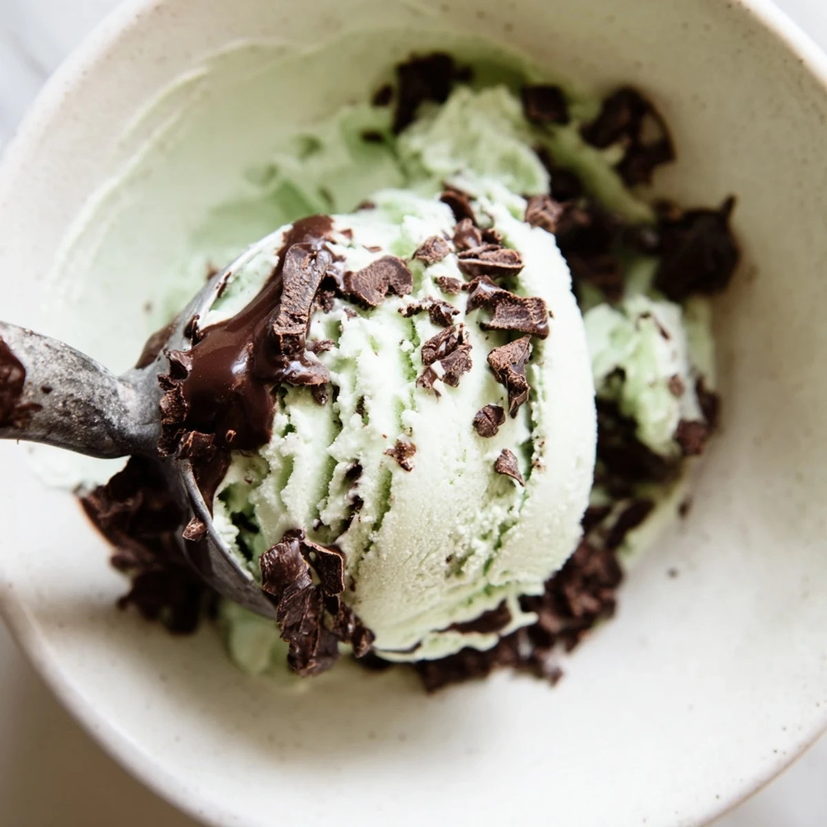 A serving of Mint Chocolate Chip Ice Cream in a waffle cone, drizzled with chocolate sauce on a sunny picnic table.