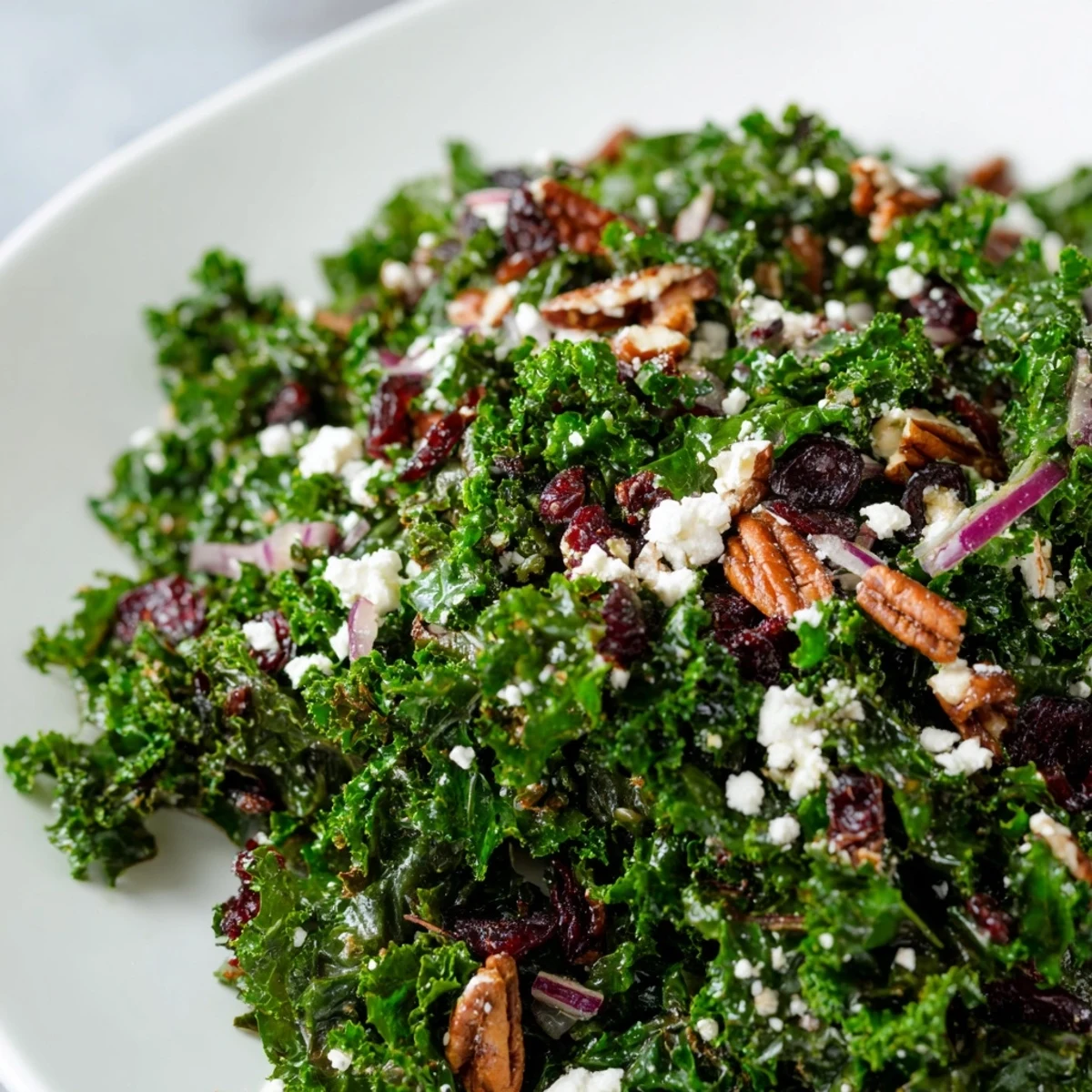 Overhead view of Winter Kale Salad with Pecans and Cranberries drizzled with maple vinaigrette, showing sliced apple and red onion accents.