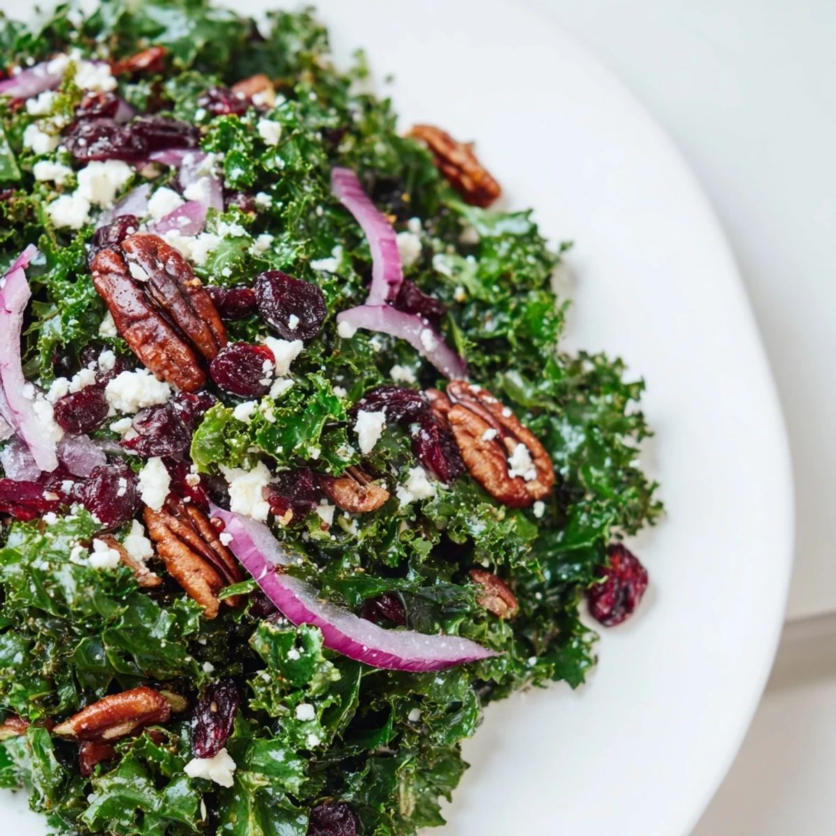 A vibrant Winter Kale Salad with Pecans and Cranberries in a white bowl, featuring massaged greens, toasted nuts, and jewel-like dried fruit.