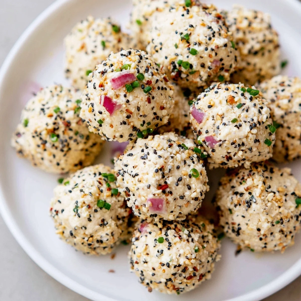 Bright serving dish holding Everything Bagel Cottage Cheese Bites, garnished with red onion and sesame seeds.