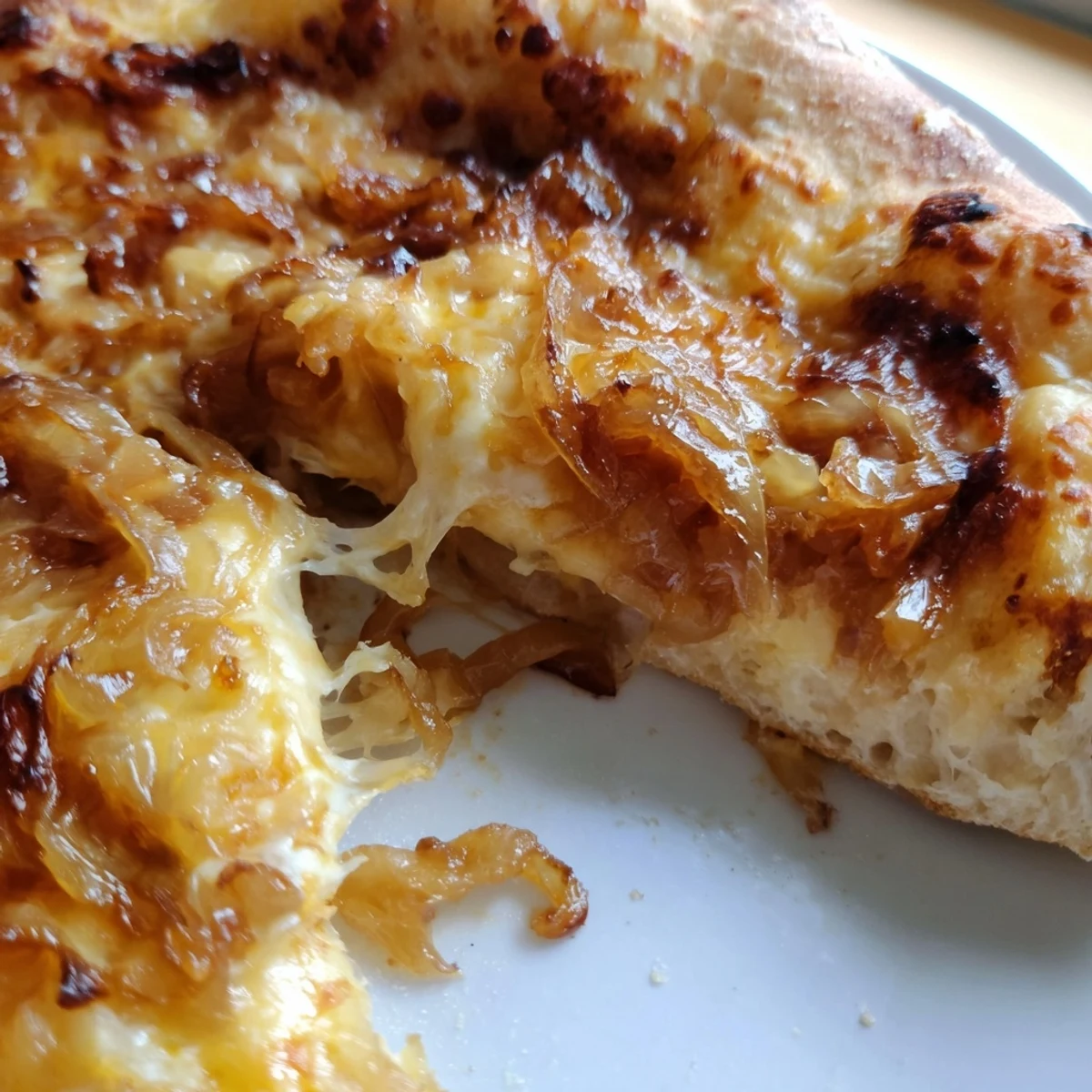 A close-up of a slice of Caramelized Onion Pizza With Melty Cheese showing gooey cheese pull and caramelized onion strands, with fresh arugula garnish.