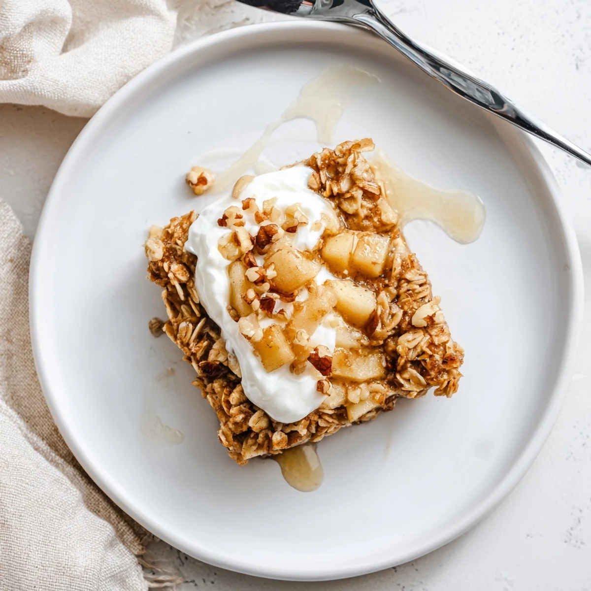 Golden-brown baked apple oatmeal with Greek yogurt topped with a creamy dollop and chopped walnuts.