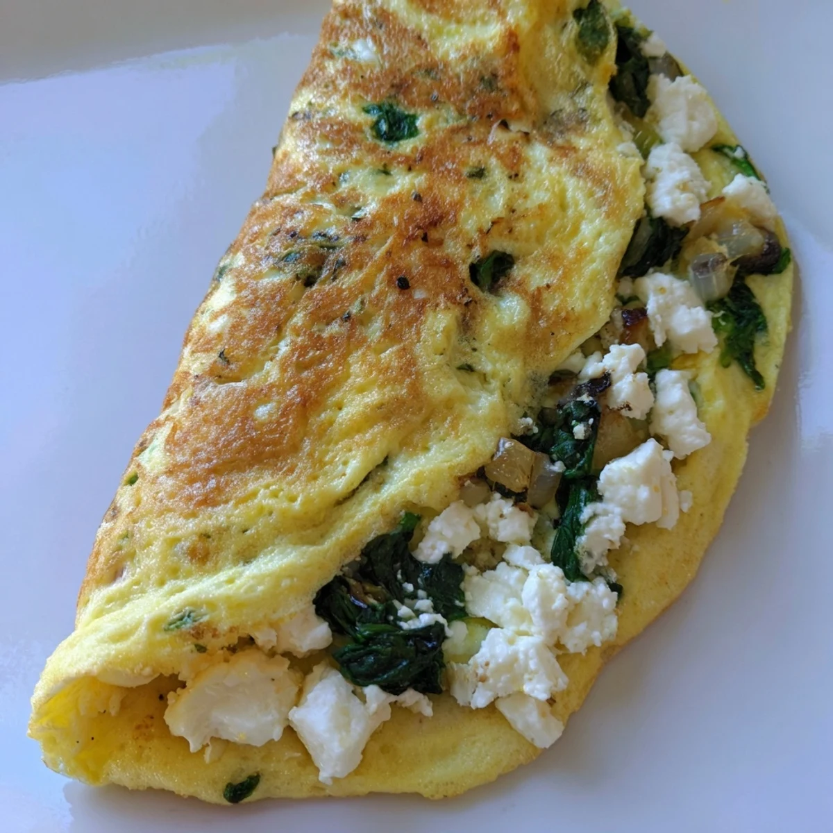 Freshly cooked 15-Minute Spinach and Feta Omelet, folded golden eggs with wilted greens and crumbled cheese on a plate.