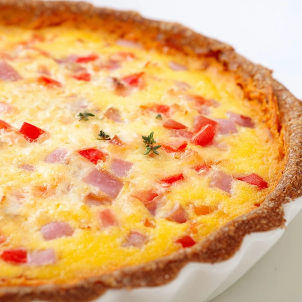 A vibrant slice of Red Capsicum and Ham Quiche with Sweet Potato Crust showcases golden eggs and diced red peppers atop a rustic orange crust.