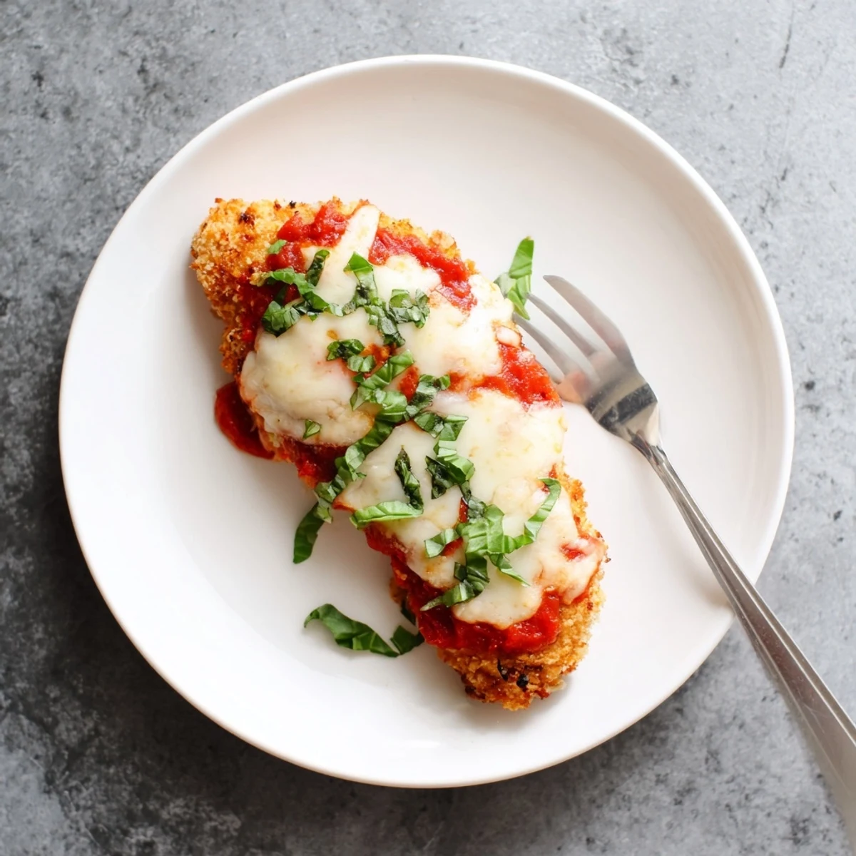 Golden fried Chicken Parmigiana breasts topped with bubbly mozzarella and rich tomato sauce, served on a plate with spaghetti.