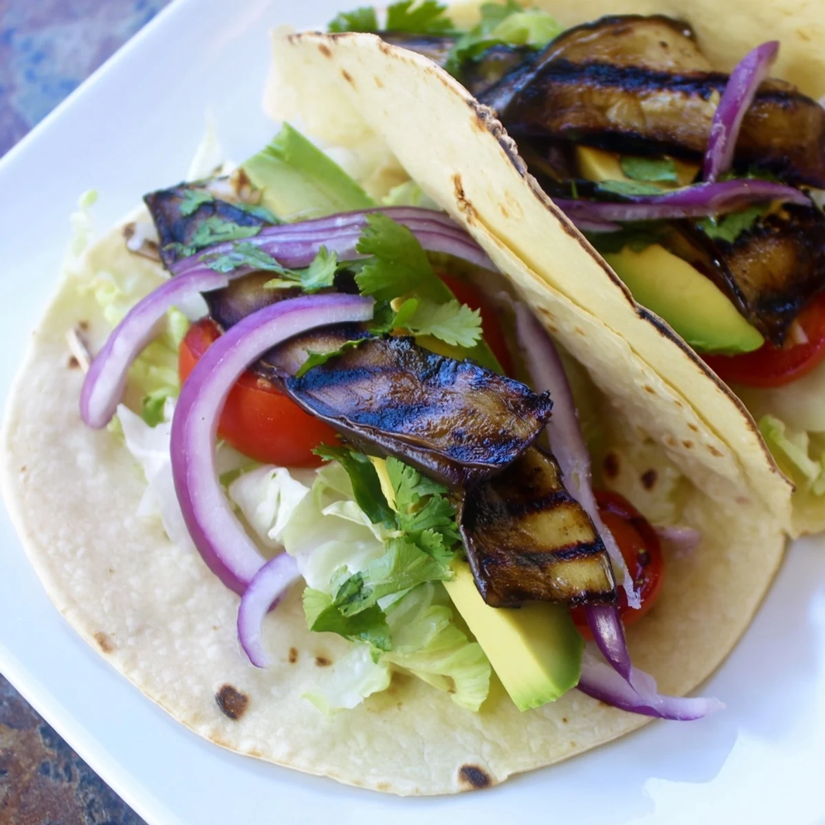 Charred Eggplant Tacos with smoky grilled eggplant, fresh lettuce, and avocado on warm corn tortillas.