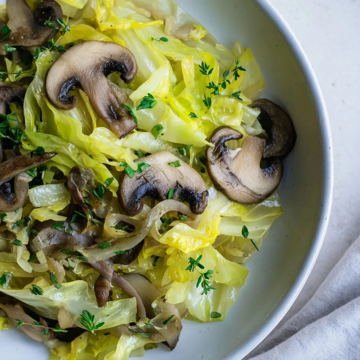 Steamed green cabbage and earthy mushrooms are sautéed in a pan with onion and fresh thyme.
