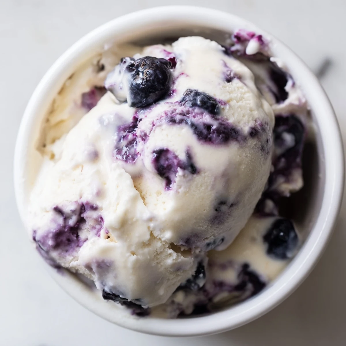 Creamy Blueberry Cottage Cheese Ice Cream scooped into a bowl, topped with fresh blueberries and a mint sprig.