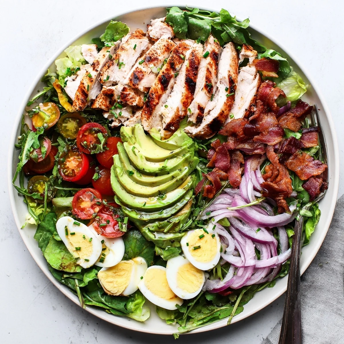Crispy bacon and quartered hard-boiled eggs garnish the hearty Paleo Grilled Chicken Cobb Salad With Honey Dijon Dressing, drizzled with a tangy, sweet dressing.