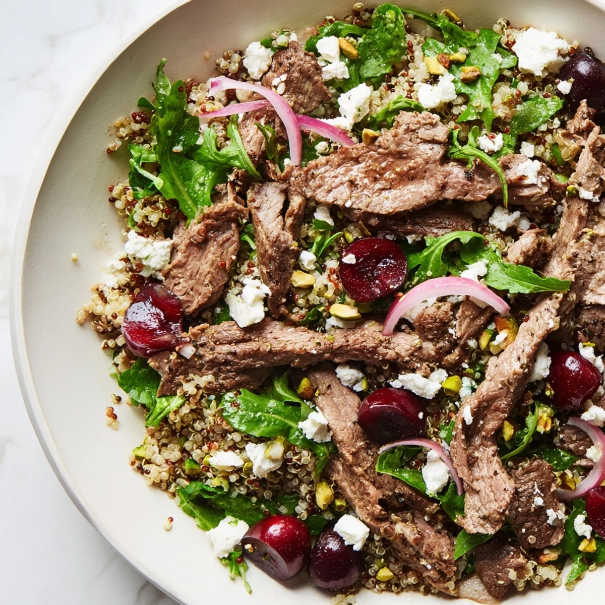 Protein-rich cherry quinoa salad with lamb featuring spiced strips, juicy red cherries, and crumbled feta cheese topping