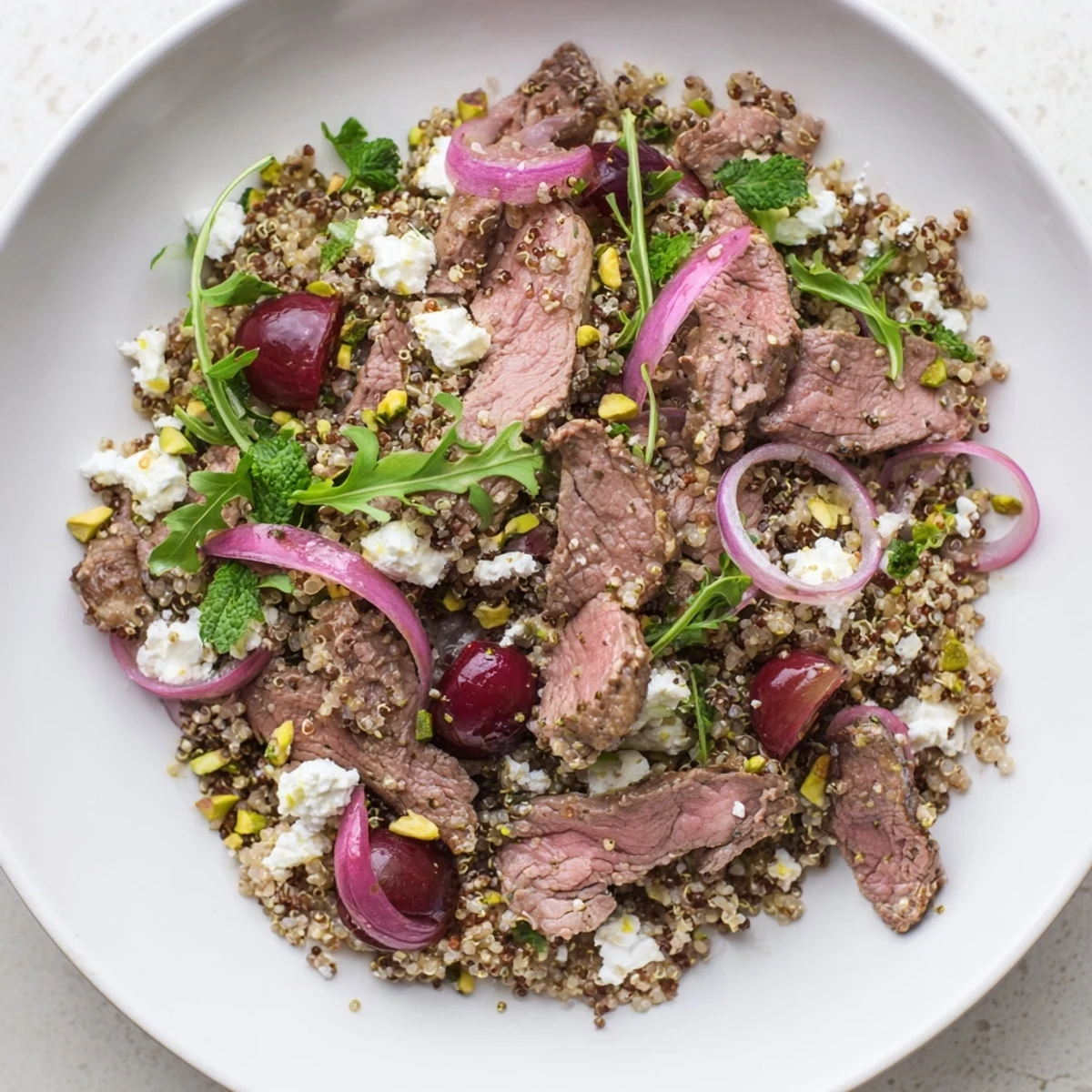 Mediterranean-style cherry quinoa salad with lamb displayed with toasted pistachios, leafy greens, and bright herb garnish
