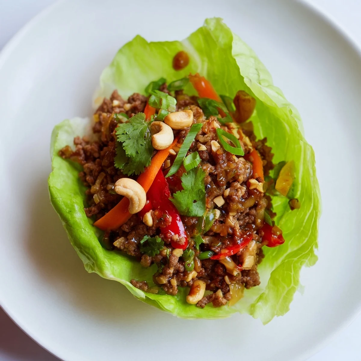 Platter of Asian-style beef and cashew lettuce cups topped with colorful vegetables and lime wedges for serving