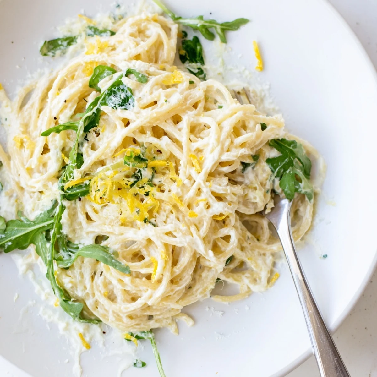 Creamy lemon ricotta pasta tossed with fresh arugula in a white ceramic bowl