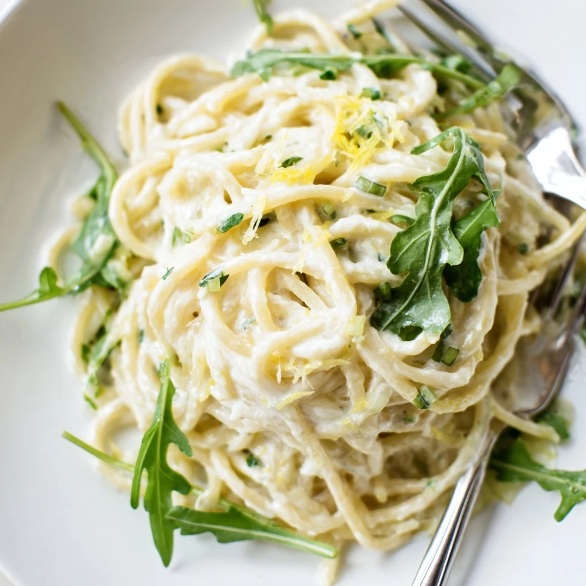 Twirled spaghetti with bright lemon ricotta sauce and wilted arugula on a rustic plate