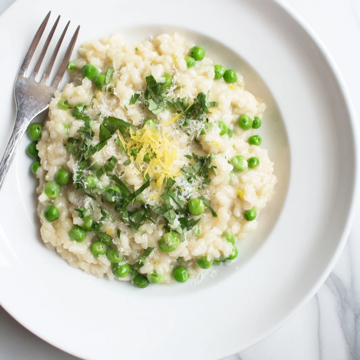 Vibrant green pea risotto garnished with parsley and lemon zest in a shallow white bowl