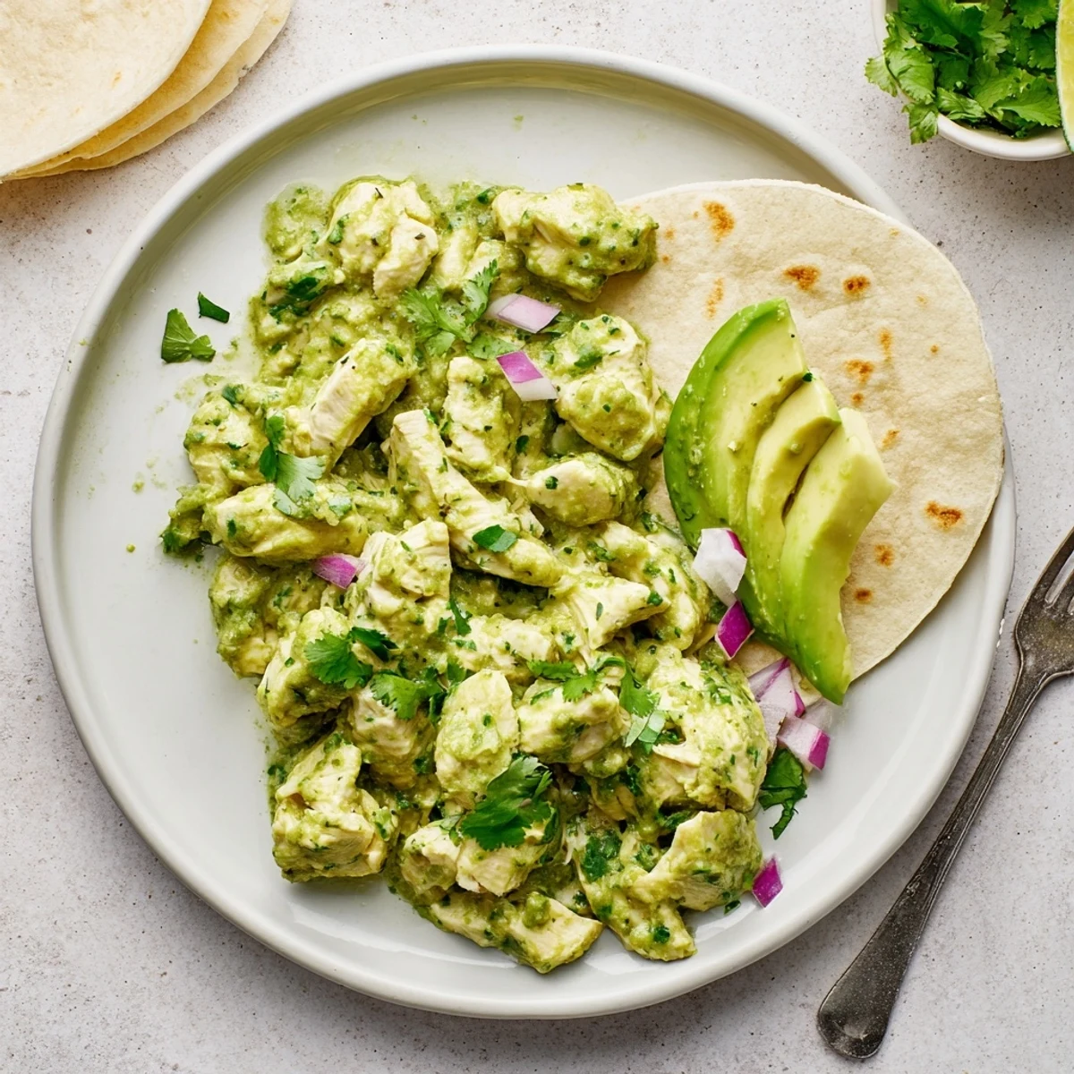 Shredded chicken thighs simmered in vibrant green salsa verde sauce, garnished with fresh cilantro.
