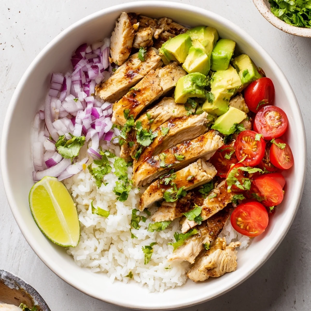 Colorful rice bowl showcasing tender honey-lime marinated chicken topped with ripe avocado chunks cherry tomatoes and red onion