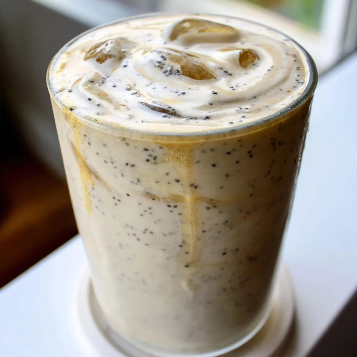 Golden Greek yogurt banana smoothie poured into a glass with a straw on a wooden table