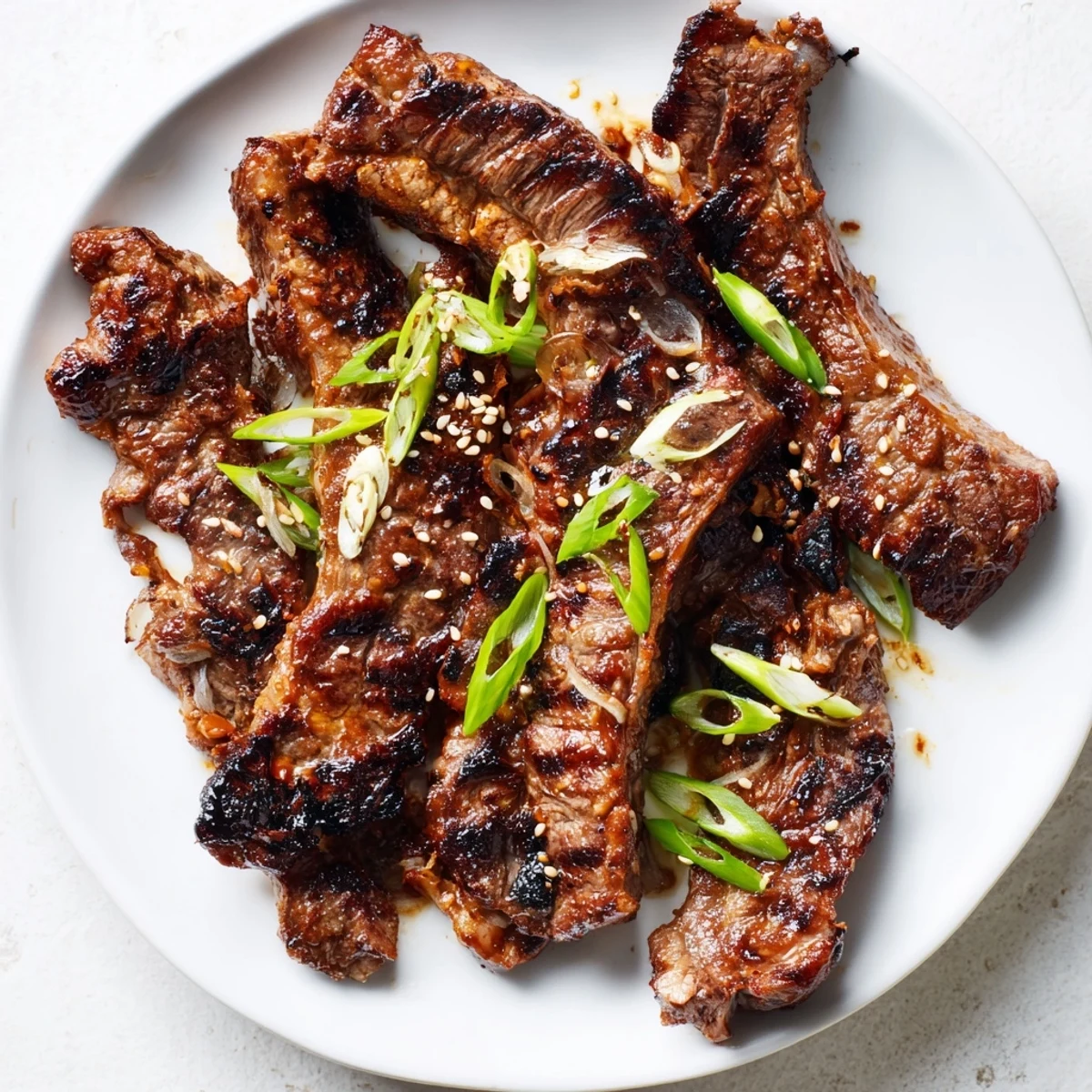 Golden Korean galbi grilled ribs with caramelized char marks and sesame seed garnish on a white plate