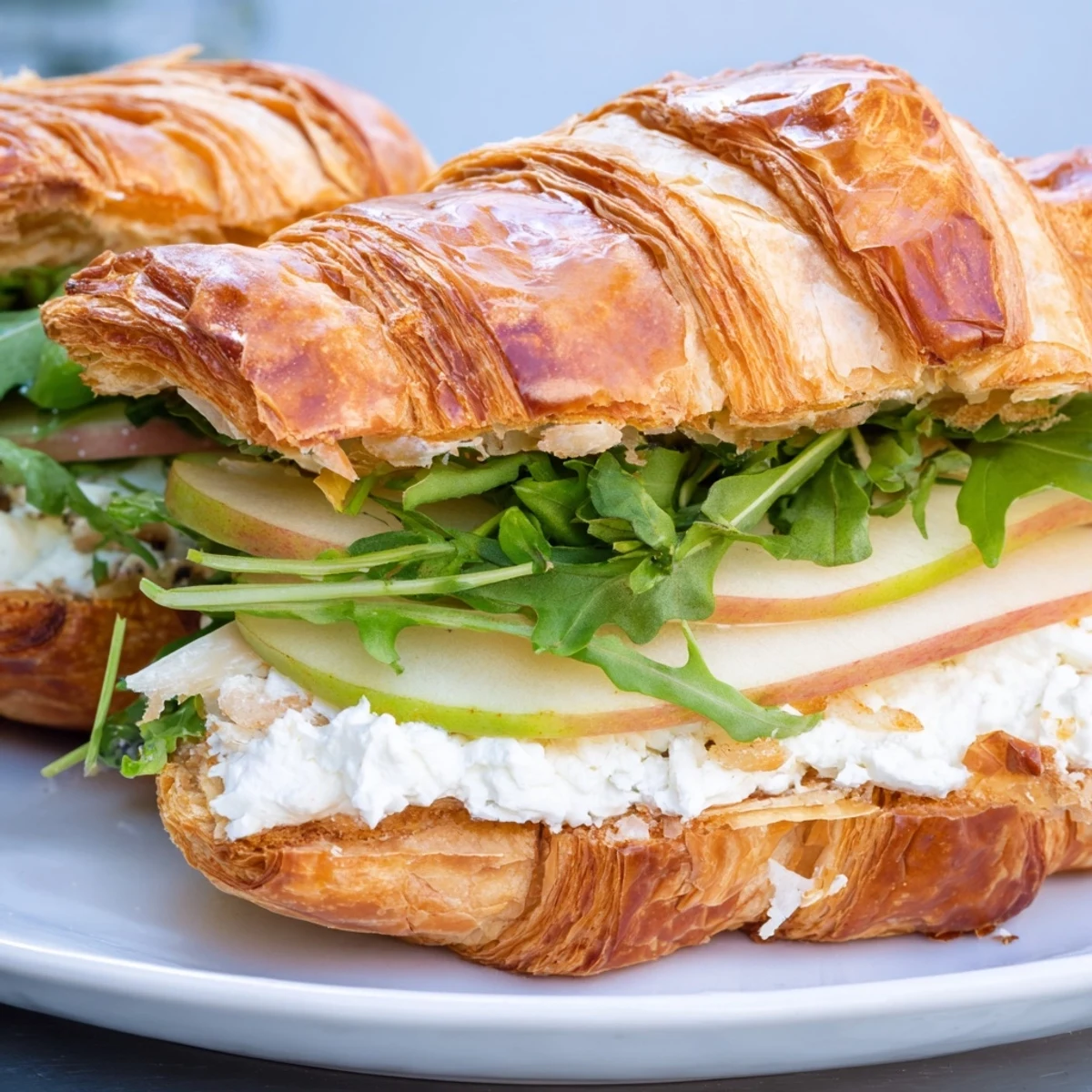 Golden Apple Goat Cheese Croissant Sandwich with fresh arugula on wooden board