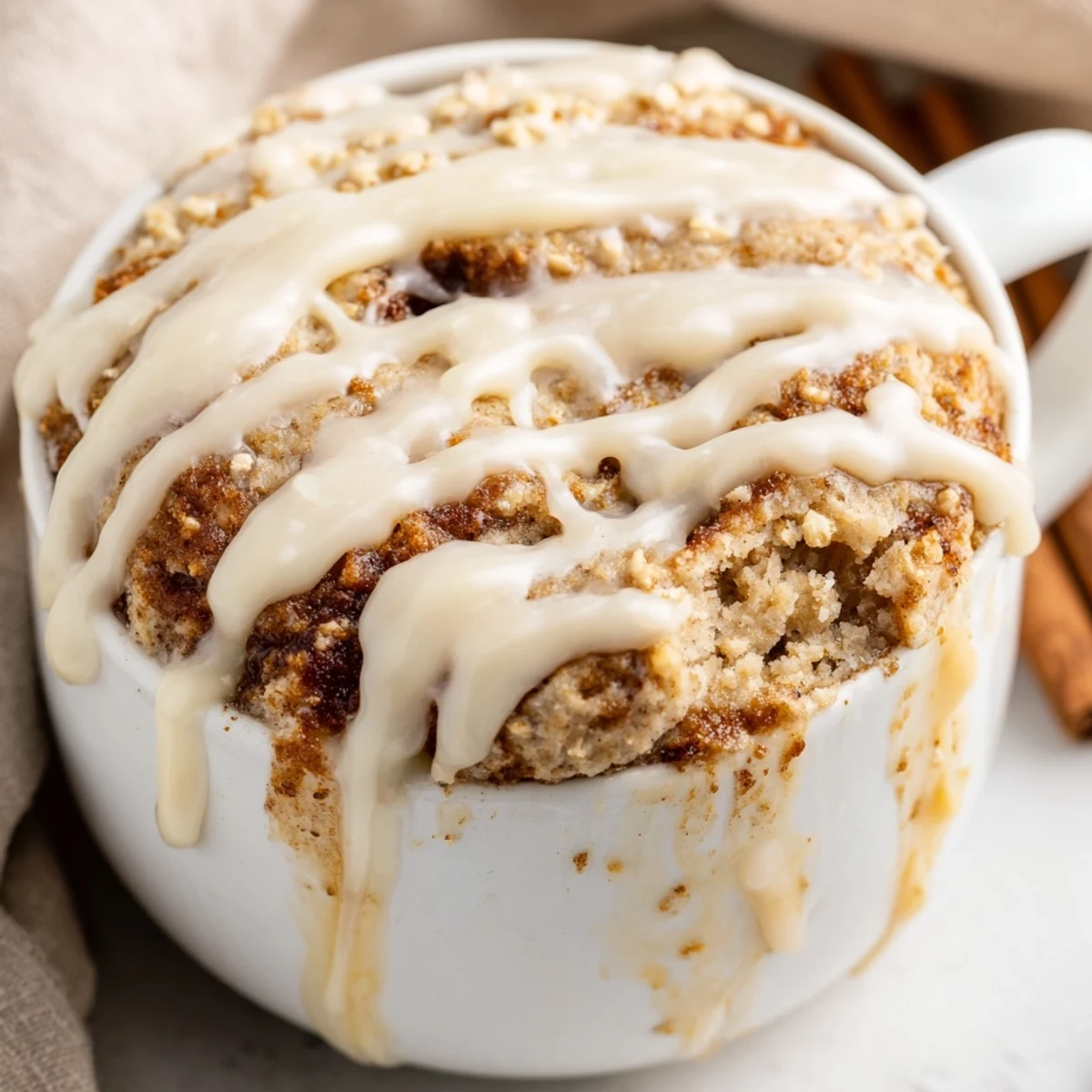Fluffy single-serve cinnamon roll mug cake topped with creamy glaze and dusted with ground cinnamon