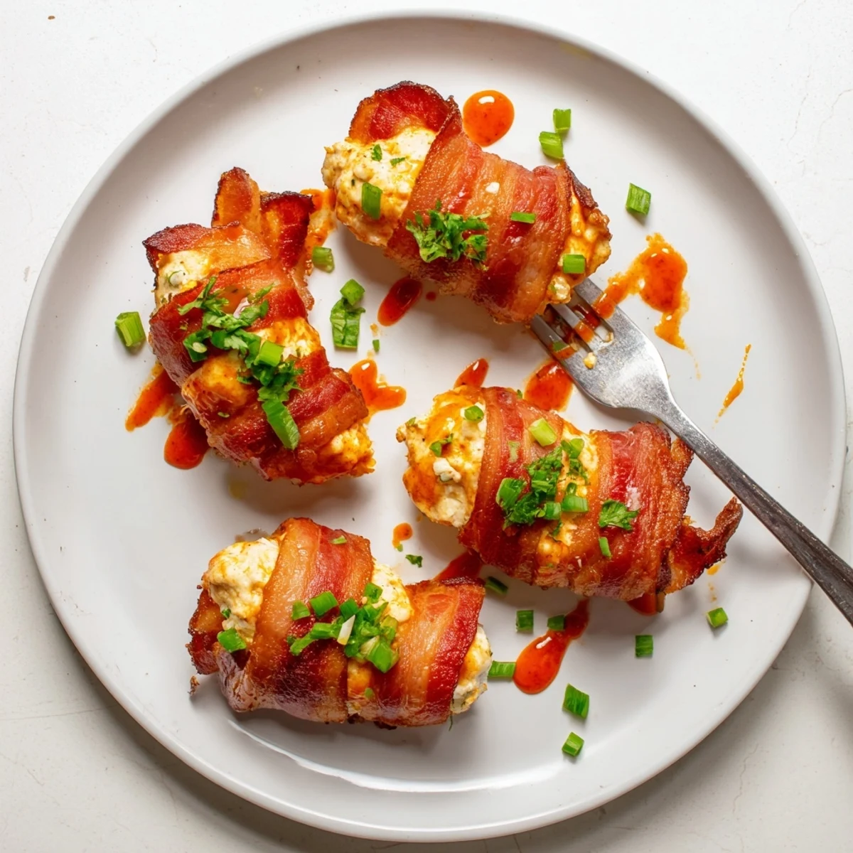 Crispy bacon-wrapped Buffalo Chicken Bombs oozing with spicy cheese filling on a white platter