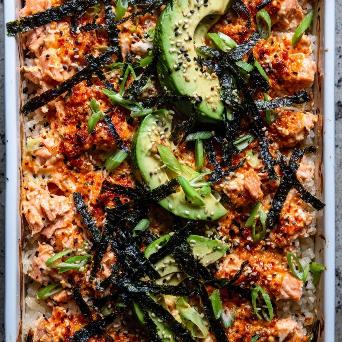 Baked salmon sushi casserole topped with nori strips green onions and toasted sesame seeds