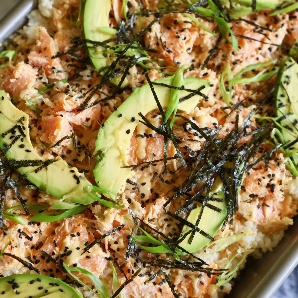 Golden salmon sushi bake with creamy spicy mayo and fresh avocado slices on seasoned rice