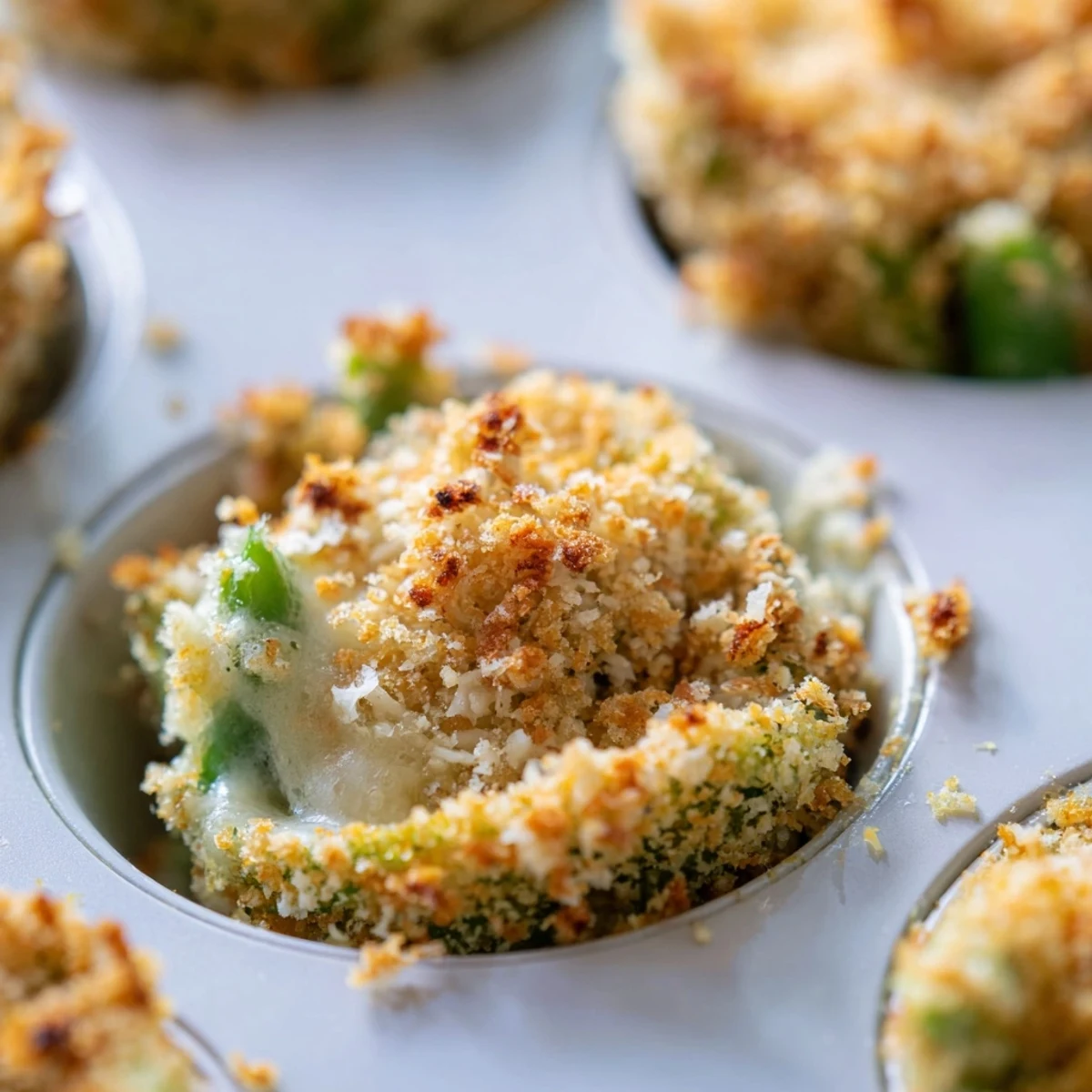Individual muffin-sized green bean casserole portions topped with melted Parmesan and golden breadcrumbs