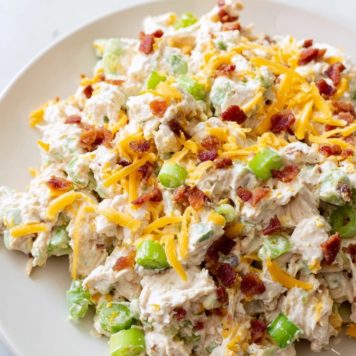 Creamy jalapeno popper keto chicken salad served in a white bowl with crispy bacon bits sprinkled on top