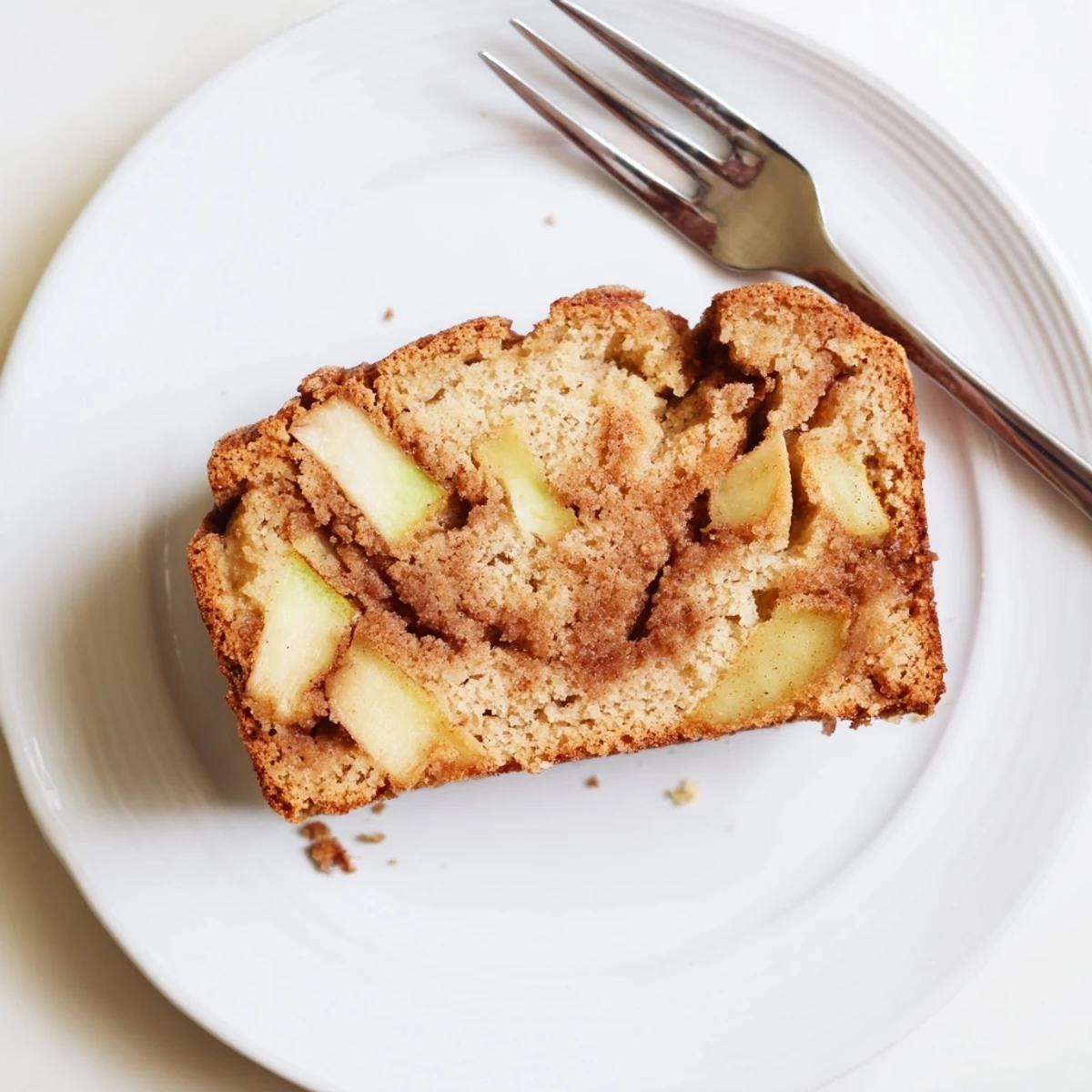 Golden loaf of cinnamon apple bread topped with sparkling sugar and tender diced apple pieces