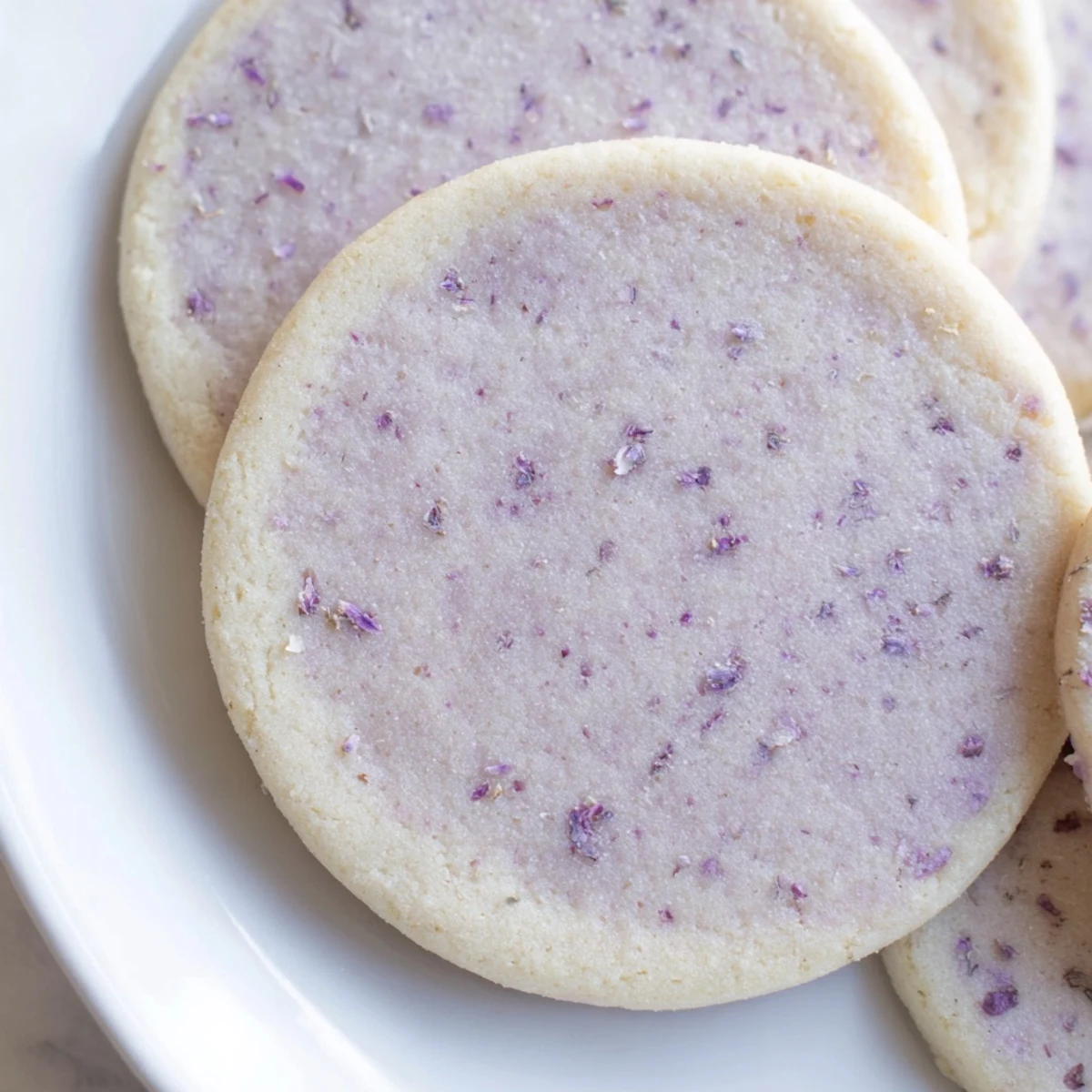 Buttery lilac sugar cookies arranged on a rustic white ceramic serving plate
