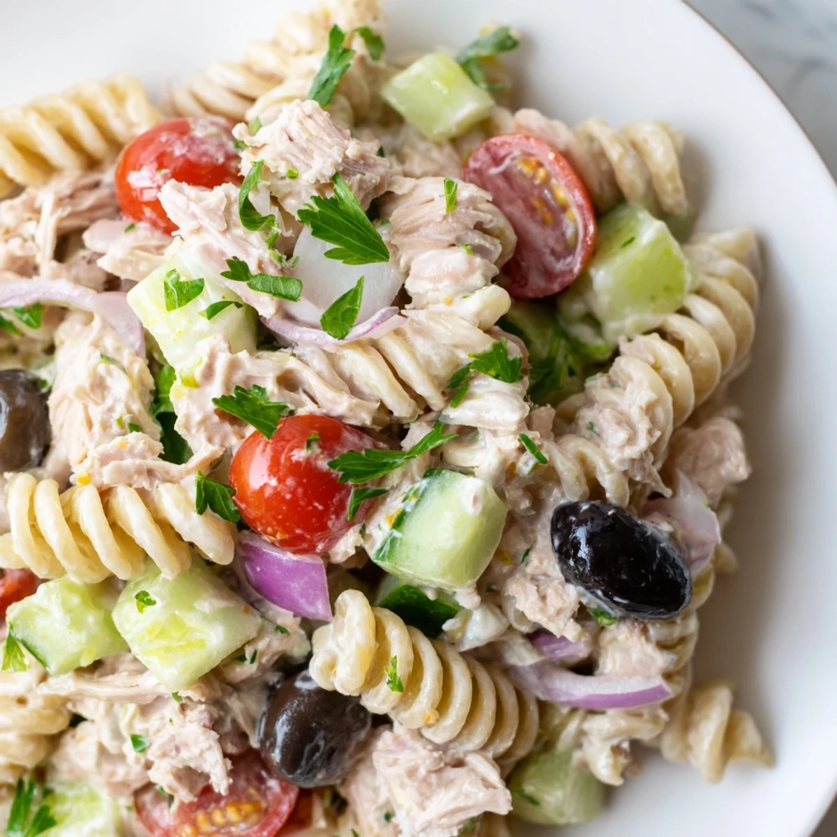 Chilled tuna pasta salad topped with black olives and fresh parsley garnish