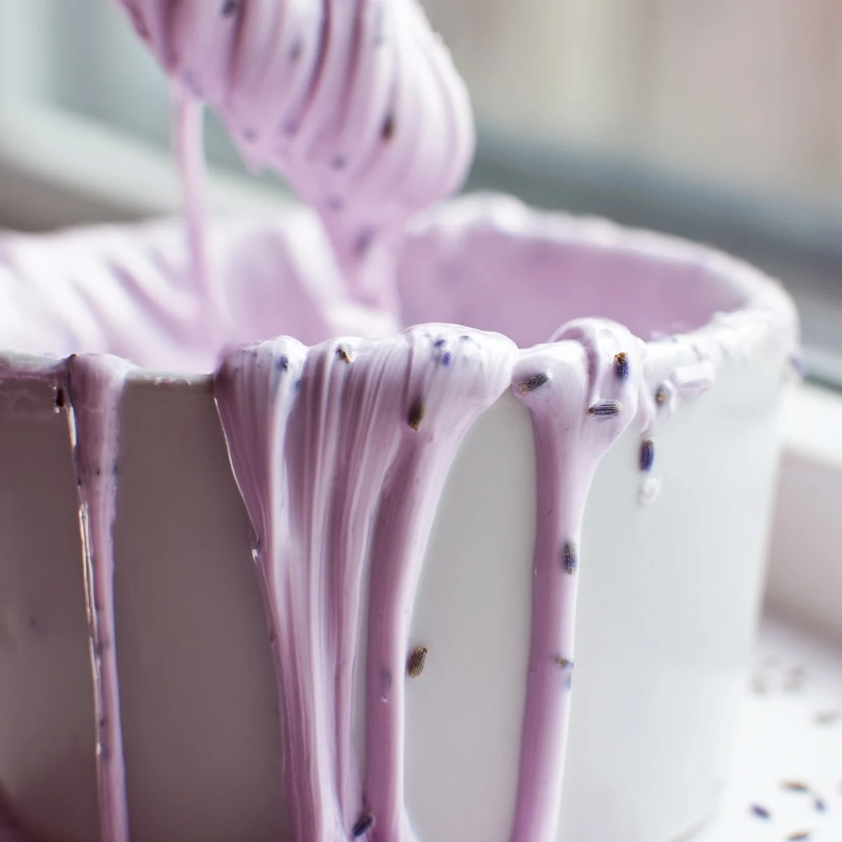 Velvety lavender glaze dripping off golden scones on a rustic white ceramic plate