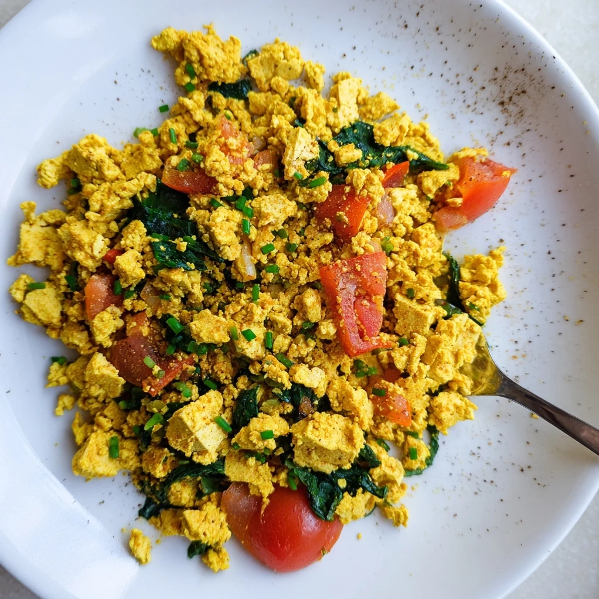 Tofu Scramble with sauteed peppers and wilted spinach, steaming on plate