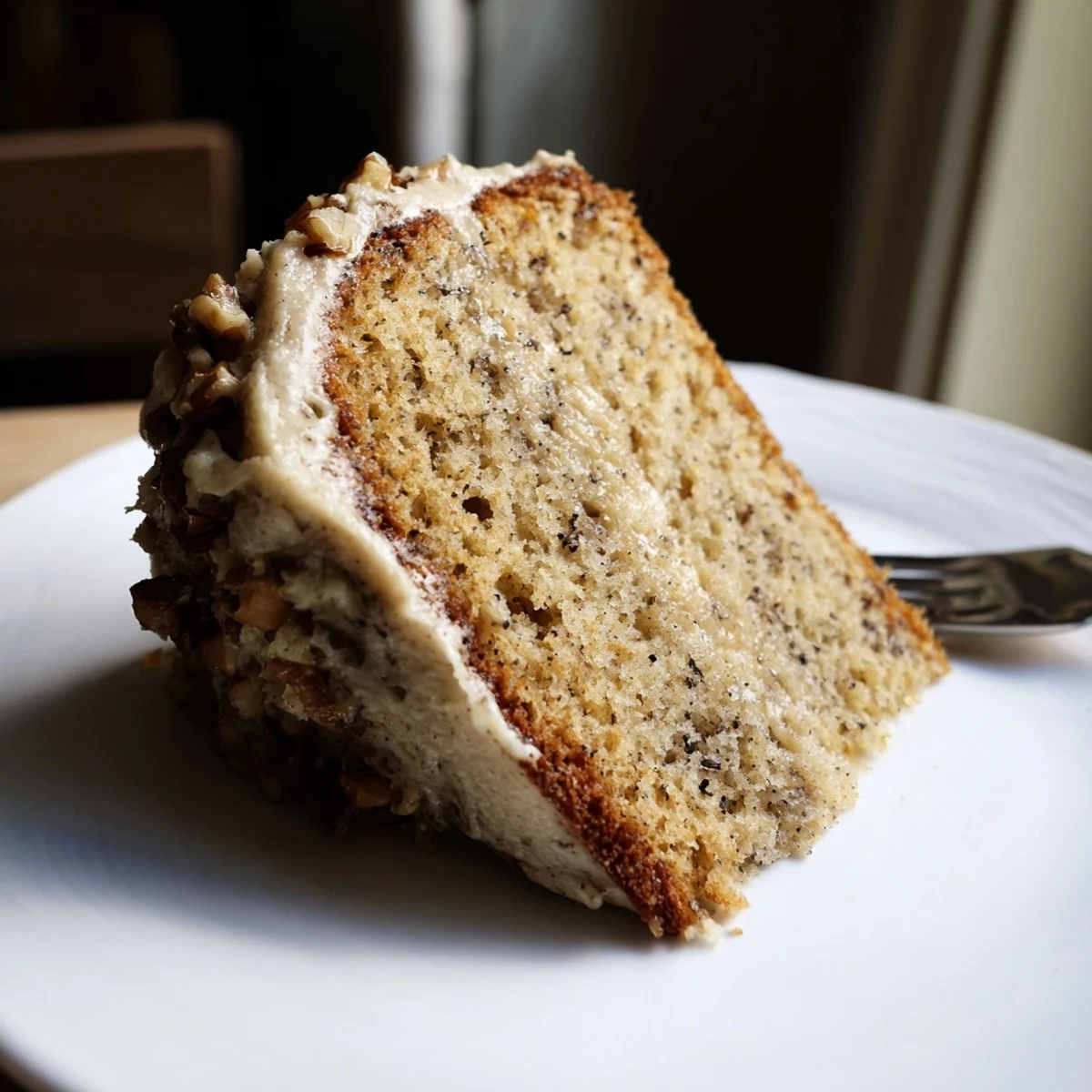 Slice of Moist Banana Cake topped with cream cheese frosting, nutty crunch.