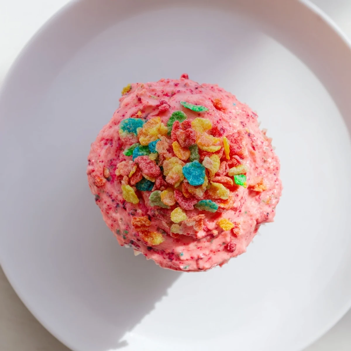 Fluffy pink buttercream frosting swirled with crushed Fruity Pebbles on a vanilla cupcake