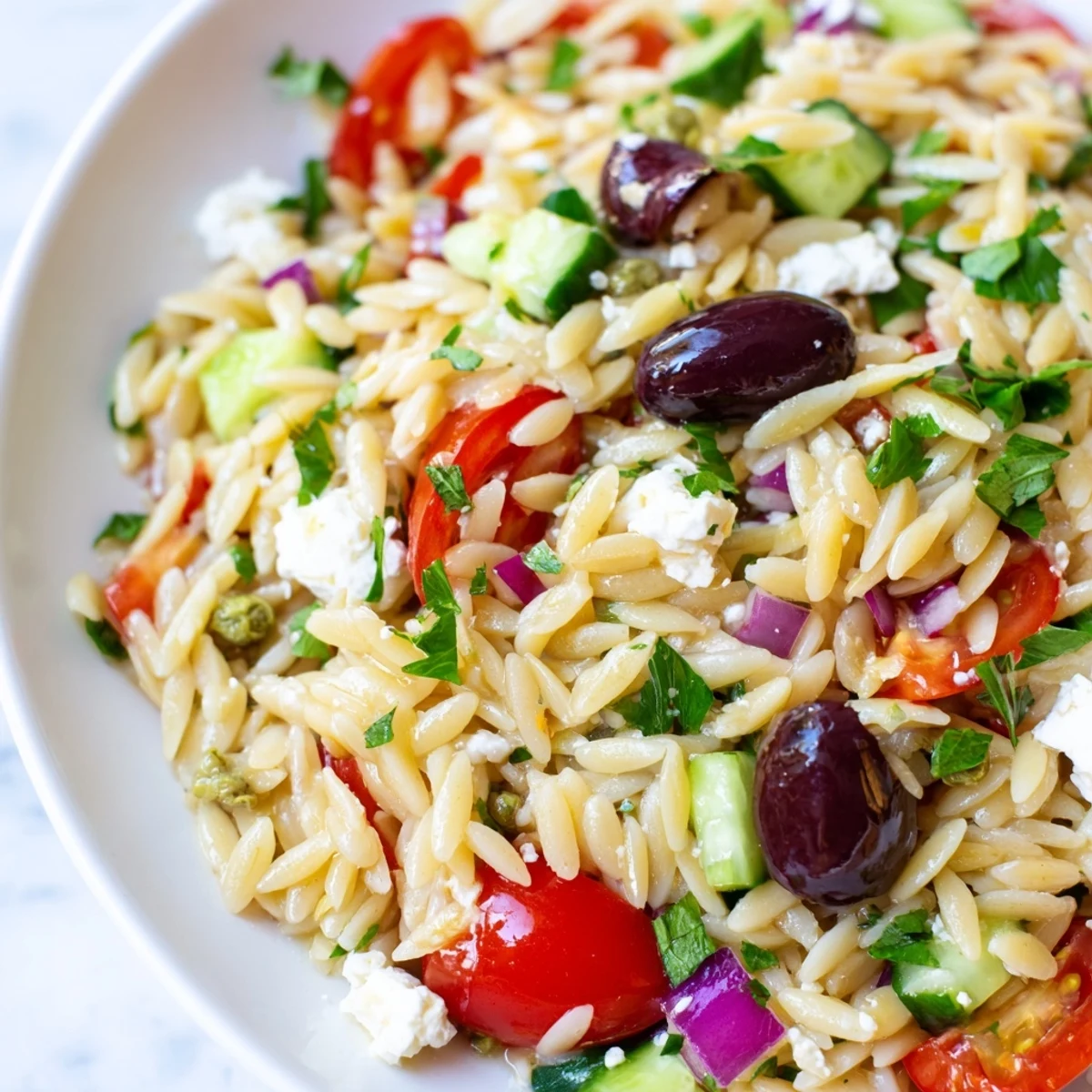Bright Juicy Mediterranean Orzo Pasta Salad topped with crumbled feta on a sunny patio table