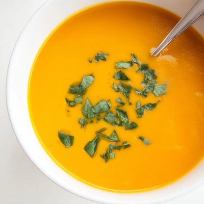 Silky, bright orange carrot soup topped with chopped coriander and accompanied by bubbly, crisp Parmesan bread slices.