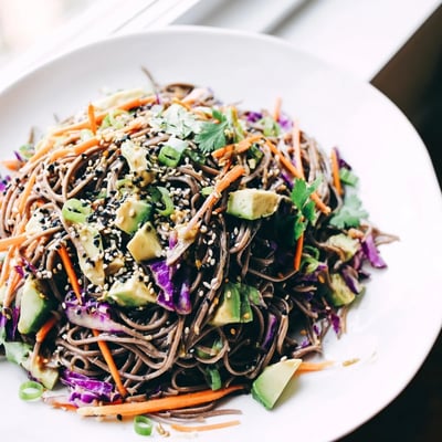 A close-up of the vibrant Sesame Avocado and Soba Noodle Salad shows creamy avocado slices and crisp veggies in a serving bowl.